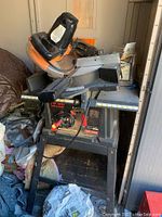 Craftsman 10 inch table saw with Chicago Electric compound miter saw on top and various tools and cloths surrounding in a storage or workshop space.