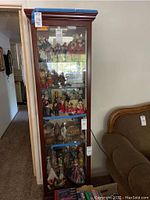 Full front view of the tall dark wood curio cabinet with glass front and multiple shelves containing various collectibles. Shows overall size and design of cabinet.