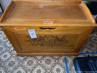 Front view of the wooden shoe storage bench showing floral carvings on the panel and scratches on the top surface.