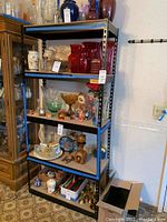 Full view of one metal shelving unit with various glass, ceramic and decorative items displayed on shelves.