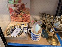 Full lot with menorahs, cookbook, decorative plate, dreidels, mug, and books arranged on a shelf.