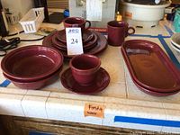 Photo showing full set of maroon Fiesta Ware including plates, bowls, cups, saucers, and two oblong serving dishes placed on a counter.