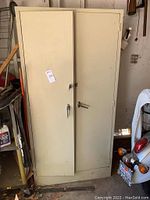 Closed beige metal storage cabinet with double doors and two handles, one with a lock. Cabinet stands about 6 feet tall.