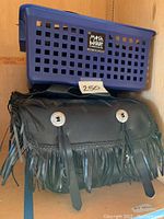 Pair of black leather fringe saddlebags with silver conchos and buckle straps under a blue plastic basket.