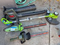 Photo showing four power lawn tools: green Greenworks weedwhacker, green Portland hedge trimmer, darker green Hedgehog hedge trimmer, and blue Sears Craftsman blower/vac, all untested.