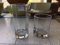 Two drinking glasses, one tall highball and one shorter old-fashioned, each with a clear octagonal base, displayed on a tiled surface.