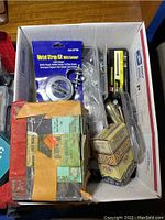 Photo showing a box containing a metal strap kit with fastener, and various boxes of hardware including nails and screws.