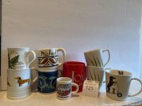 Photo showing eight assorted mugs with various sizes and designs including dogs, fish, flowers, and location names.