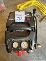 Top view of compressor showing gauge dials, on/off switch, handle, power cord, and attached yellow coiled air hose.