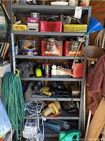 Full view of metal shelving unit filled with tools, hardware, and miscellaneous items including circular saws, cans, extension cords.