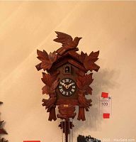 Full view of carved wooden cuckoo clock showing leaf and bird carvings, clock face, weights and chains