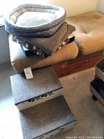 Photo showing dog steps stacked with pet bed and blankets on cushioned bench.