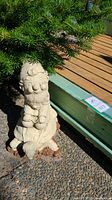 Gnome statue sitting on turtle under tree with green fence in background