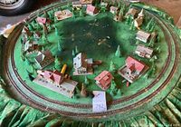 Full overhead view of the entire handmade vintage train diorama showing the circular train track, green base, miniature buildings, and trees.