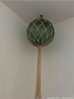 Green spherical glass float wrapped in beige rope netting, hanging from ceiling
