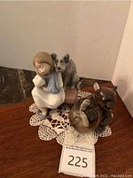 Lladro figurine of girl with dog seated on pink cushioned stool, on lace doily, with glass bear figurine.