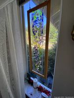 Full view of stained glass panel hanging in window framed in wood, showing flowers and birds