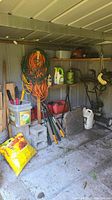 Photo of garden shed interior showing cinder blocks, coiled hoses, gardening tools and pots.