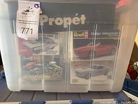 Plastic bin with multiple Revell model car kits visible including Dodge Sidewinder, 1964 Dodge 330 Super Stock, Rat Rods, and other kits.
