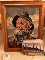 Framed fisherman tapestry with older man smoking pipe and small framed lighthouse picture in front