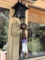 View of black outdoor lantern hanging alongside turtle wind chime and turtle thermometer mounted on wall