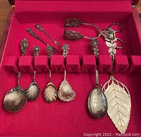 Overview of nine rose-pattern serving pieces arranged in red velvet case