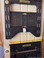 Two black folding Storehorse sawhorses mounted on a wall, with yellow top rails.