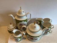 Overall set showing teapot, coffee pot, creamer, sugar bowl with lids, and tea cups, all with green floral pattern and gold detailing.