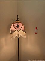 Front view of lit lamp showing pink pleated shade with fringe trim