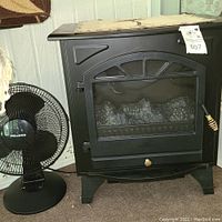 Electric stove with front view showing faux log fire and Pelonis fan to the left side, carpet flooring and textured wall