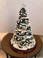 Front view of the Thomas Kinkade illuminated Christmas tree showing the full tiered village design with snow and figurines, topped with clear star.