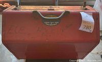 Closed red vintage metal toolbox showing 'Custom Auto Parts Speed Equipment' label and handwritten markings on front. Toolbox surface shows scratches and rust spots.
