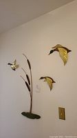 Full view of the three ducks and three cattails wall mounted decor on a beige wall showing size relation to standard wall outlet.