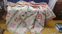 Full view of one vintage quilt showing patchwork blocks in pink, green, red, and cream tones with floral borders.