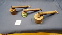 Three antique bug sprayers: two with green glass jars and one metal canister. All have rusted metal pump tubes and wooden plunger handles. Labels and graphics visible but weathered.