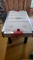 Full view of the air hockey table showing the playing surface with red paddles and hockey discs on top.