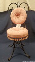 Front view of antique Victorian bent iron scroll vanity chair with pink tufted seat and backrest, showing fringe tassels and rotating base.
