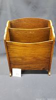 Front view of the antique oak magazine rack showing two compartments with curved top edges and wood grain finish.