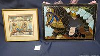 Photo showing the stained glass carousel horse artwork next to the signed carousel boy on horse print. The stained glass piece measures 29 x 20 inches and has a pink ribbon hanger. The print measures approximately 18.5 x 17.5 inches and is framed in gold with some frame scuffs.