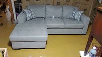 Front view of light gray fabric sofa with chaise lounger on left side and two decorative pillows.