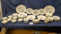 Full view of vintage Marcrest MCR5 pattern china set including plates, bowls, cups and serving pieces arranged on blue cloth backdrop.
