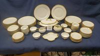 Photo showing full display of 83-piece Limoges France Old Abbey china set including plates, bowls, saucers, teacups, and serving pieces with gold accent edges.