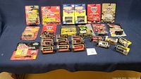 Lot of 24 various Hot Wheels style toy cars in original unopened packaging displayed together on table with blue cloth.