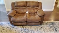Front view of brown microfiber loveseat with dual power recliners, seating cushions and armrests visible, in upright position.