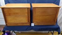Front view of two matching vintage maple nightstands side by side showing smooth wooden drawer fronts without handles.