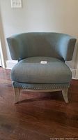Full front view of teal Mid Century Modern chair, showing curved back, cushioned seat, and nailhead trim.