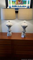 Front view of the matching pair of French Country style pottery lamps on a wooden dresser with beige fabric drum shades.