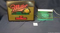 Full view of both Miller Beer and Guinness light up signs placed on a dark cloth background.