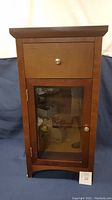 Front view of wooden cabinet with closed drawer and glass front door