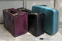 Side view of burgundy leather case, black leather case, and blue Samsonite case side by side on a table